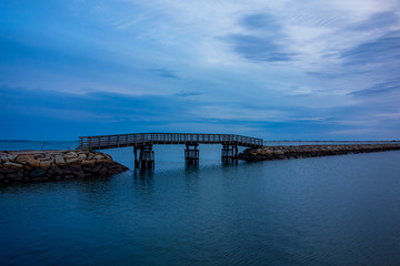 Fototapeta na wymiar Plymouth wooden bridge on rock jetty during blue hours.