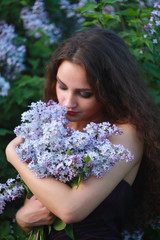 A woman dressed in a beautiful purple dress on a background of lilac bushes with a bouquet of lilac in the hands of spring.