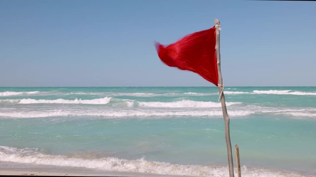 Red warning flag flutters in strong wind on a beach to alert people not to swim