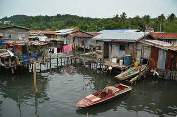 Obraz premium Stilt houses and cabins in a floating village scene with laundries drying on a washing line and small boats moored beside a boardwalk on Borneo river