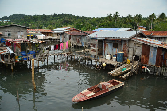 Stilt houses and cabins in a floating village scene with laundries drying on a washing line and small boats moored beside a boardwalk on Borneo river