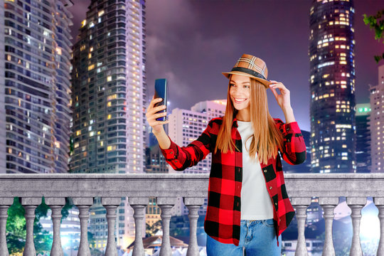 Young beautiful blonde woman in hat with smartphone on the night street. Urban portrait. Blogging concept.
