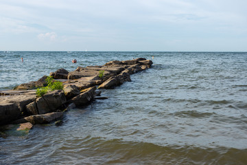 Fototapeta premium A rocky road among the lake. Summer landscape with a lake, waves breaking on the shore and a blue cloudless sky.
