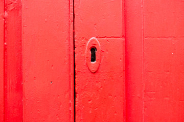 Key hole in bright red closed door, close up detail.