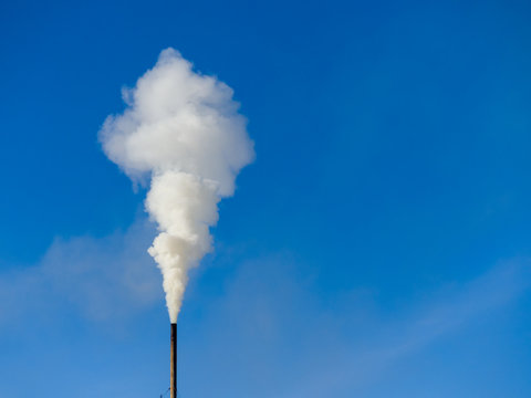 White smoke comes out of a black chimney in the blue sky. Ecology theme
