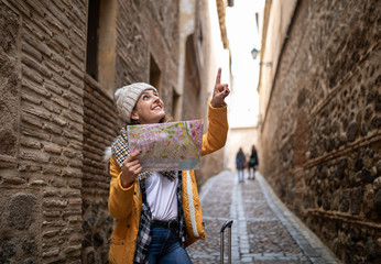 young girl sightseeing through the streets of a city with yellow coat, wool cap and suitcase