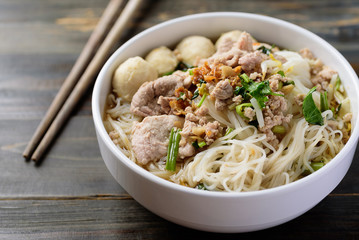 Rice noodles soup with pork and meat ball in a bowl and chopsticks on wooden background, Asian food