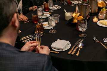Hands holding three forks at a dinner table. - obrazy, fototapety, plakaty