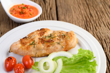Grilled chicken on a white plate with tomatoes, salad, onion and chili sauce.