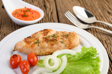 Grilled chicken on a white plate with tomatoes, salad, onion and chili sauce.