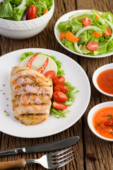 Grilled chicken on a white plate with tomatoes, salad, onion, chili and sauce.