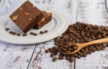 Chocolate brownies on a white plate and coffee beans on a wooden spoon.