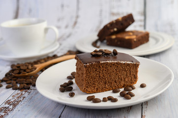 Chocolate cake on a white plate and coffee beans on a wooden spoon on a wooden table.