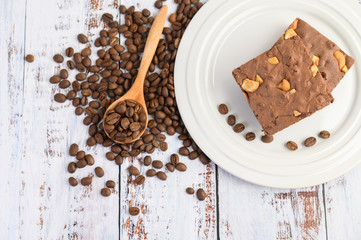 Chocolate brownies on a white plate and coffee beans on a wooden spoon.
