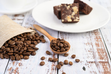 Coffee beans on wooden spoon and hemp sacks on a white wood table.