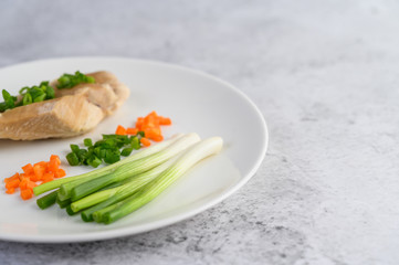 Steamed chicken breast on a white plate with spring onions and chopped carrots