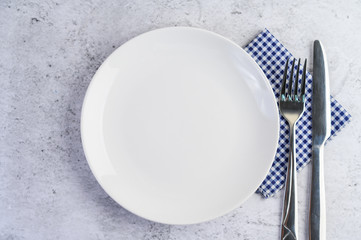 White empty plate with fork and a knife on a blue-white tablecloth.