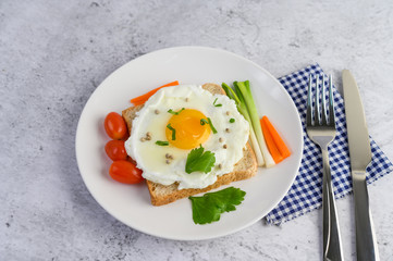 A fried egg laying on a toast, topped with pepper seeds with carrots and spring onions.