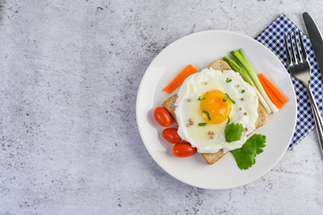 A fried egg laying on a toast, topped with pepper seeds with carrots and spring onions.