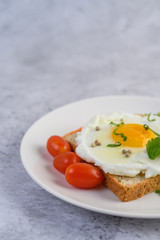 A fried egg laying on a toast, topped with pepper seeds with carrots and spring onions.