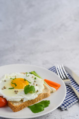 A fried egg laying on a toast, topped with pepper seeds with carrots and spring onions.