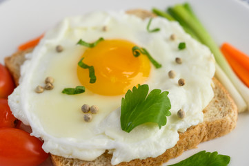 A fried egg laying on a toast, topped with pepper seeds with carrots and spring onions.