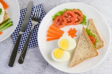 Boiled eggs, bread, carrots, and tomatoes on a white plate with a knife and fork.