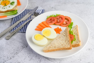 Boiled eggs, bread, carrots, and tomatoes on a white plate with a knife and fork.