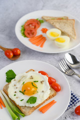 A fried egg laying on a toast, topped with pepper seeds with carrots, baby corn and spring onions.