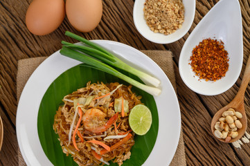 Padthai shrimp in a white dish with lime and eggs on wooden table.
