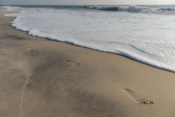 Footprints on sand about to get washed by the waves