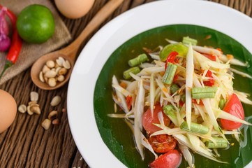 Papaya Salad (Som tum Thai) on a white plate on a wooden table.