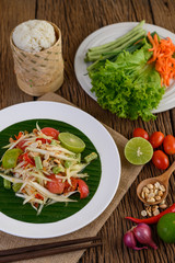 Papaya Salad (Som tum Thai) on a white plate on a wooden table.