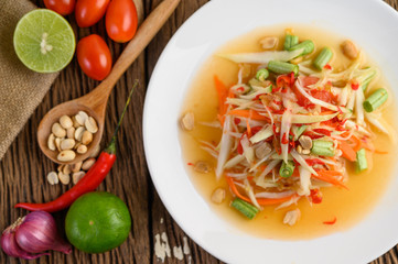 Papaya Salad (Som tum Thai) on a white plate on a wooden table.