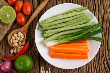 Thai style spicy food, Som Tum food concept, props decoration Garlic, lemon, tomatoes, chili, long-hatched beans, spring onions, shallots,  and carrots and peanuts on wood spoon on wood table.