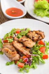 Grilled chicken on a white plate with a salad of tomatoes, carrots and chilies cut into pieces.