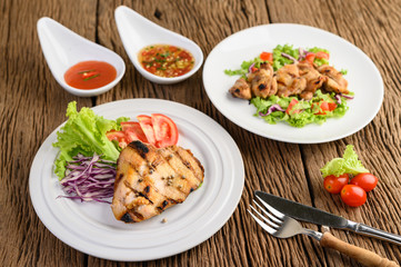 Grilled chicken on a white plate with a salad of tomatoes, carrots and chilies cut into pieces.