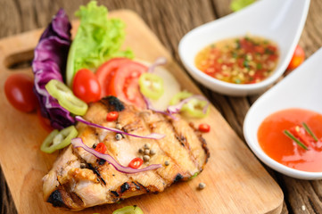 Fototapeta na wymiar Grilled chicken on a Wood cutting board with salad, tomatoes, chilies cut into pieces, and sauce.