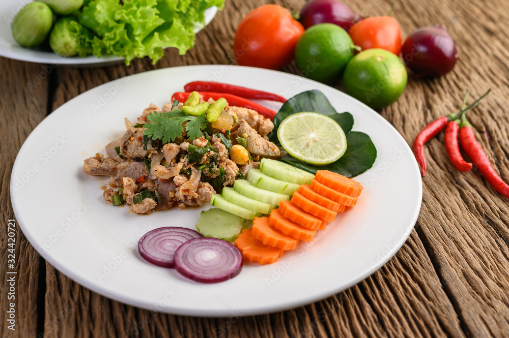 Wall mural spicy minced pork salad on a white plate on wooden table.