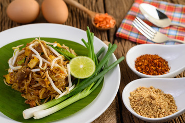Pad Thai in a white plate with lemon, eggs and seasoning on a wooden table.