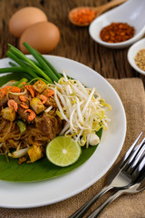 Pad Thai in a white plate with lemon, eggs and seasoning on a wooden table.
