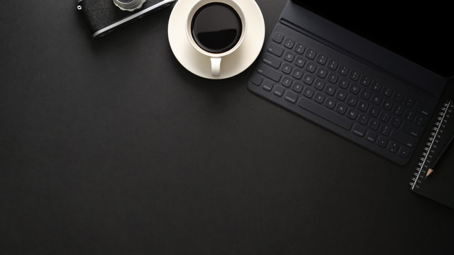 Top view of workplace with wireless keyboard, copy space, camera and coffee cup on black table