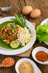 Pad Thai in a white plate with lemon, eggs and seasoning on a wooden table.