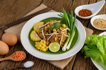 Pad Thai in a white plate with lemon, eggs and seasoning on a wooden table.