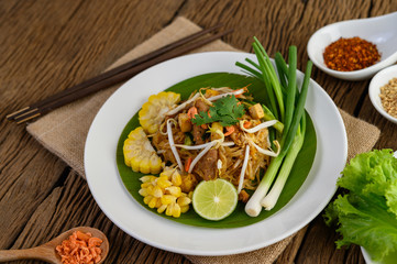 Pad Thai in a white plate with lemon, eggs and seasoning on a wooden table.