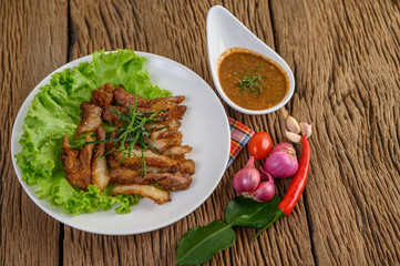 Pork neck grilled on a white plate wiht red onion, tomato, and chili on the wooden table.
