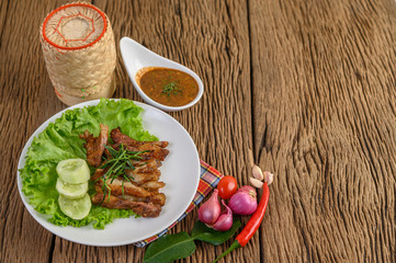 Pork neck grilled on a white plate wiht red onion, tomato, and chili on the wooden table.