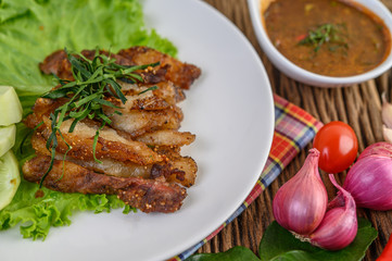 Pork neck grilled on a white plate wiht red onion, tomato, and chili on the wooden table.