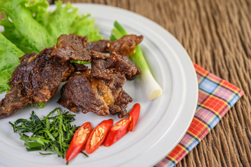 Beef fried Thai food on a white plate with spring onion, kaffir lime leaves, chilies, salad and chili paste in a cup.
