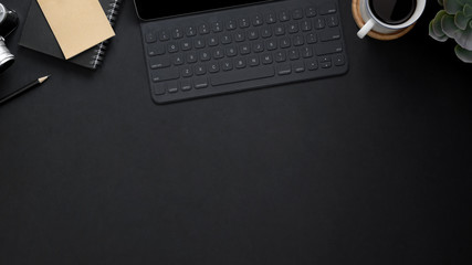 Top view of workplace with wireless keyboard, copy space, office supplies and coffee cup on black...